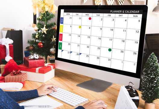 Businesswoman with calendar planner on computer screen in christmas holiday at the office with christmas decoration on table.