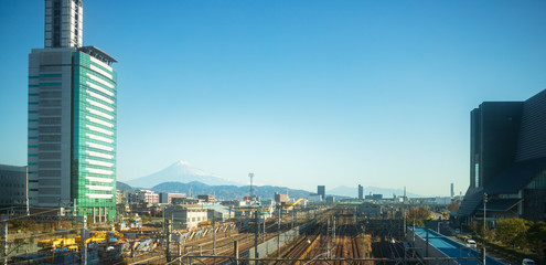 Snow covered peak of Mt. Fuji visible in distance over train tracks and urban sprawl of Shizuoka
