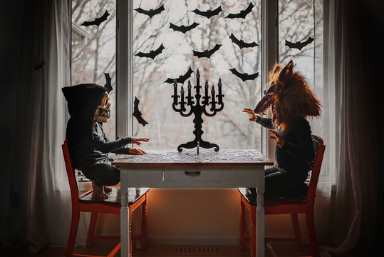Two children in Halloween costumes sitting by a window doing a jigsaw puzzle, United States