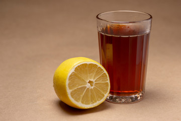 Glass with black tea and lemon on a brown background