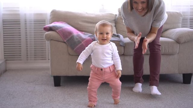 Mother clapping while baby girl is learning to walk