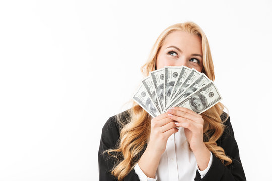 Portrait of pleased woman wearing office clothing holding fan of money, isolated over white background
