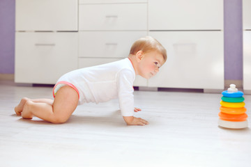 Little cute baby girl learning to crawl. Healthy child crawling in kids room. Smiling happy healthy toddler girl. Cute toddler discovering home and learning different skills