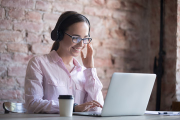 Happy businesswoman in headphones looking at laptop screen. Student listening to audio lessons....