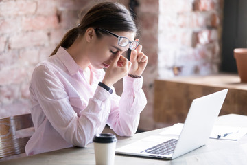 Tired worried young businesswoman holding eyeglasses, massaging nose bridge. Young woman...