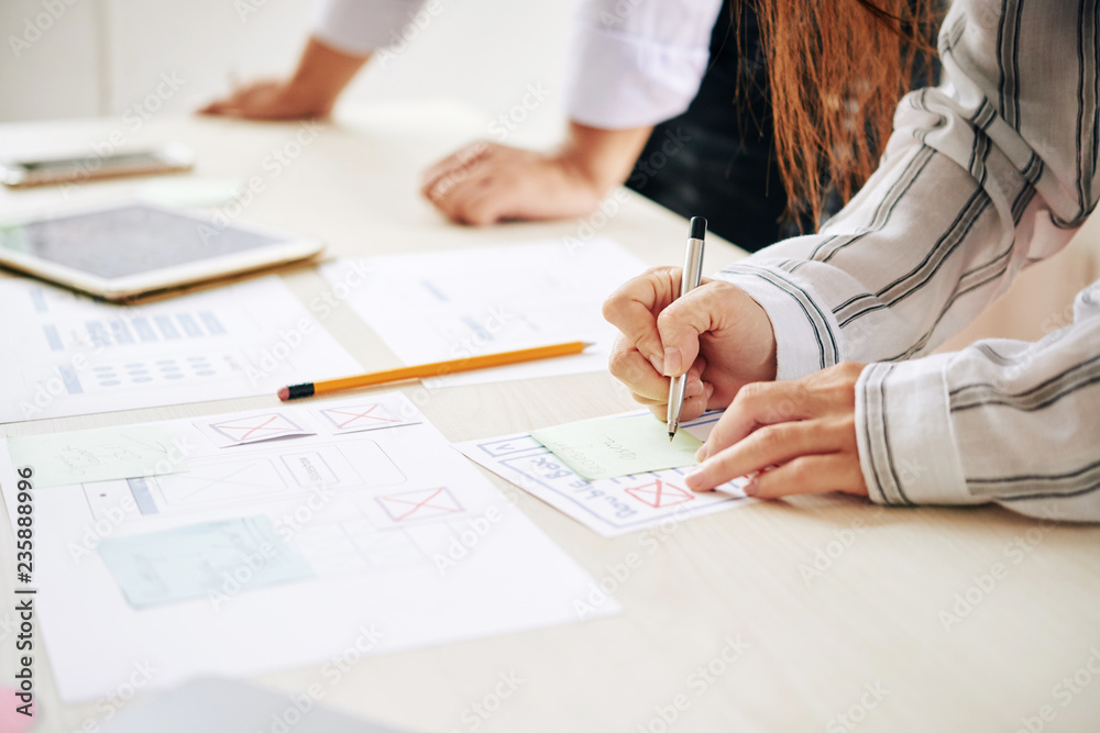 Wall mural crop shot of woman taking notes on sticker while working with man in team at table creating modern d