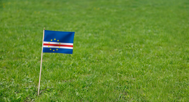 Cape Verde flag. Photo of Cape Verde flag on a green grass lawn background. Close up of national flag waving outdoors.