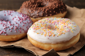 Assorted sweet donuts with icing and dressing close-up on a brown wooden table.