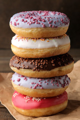 Assorted sweet donuts stacked on a brown wooden table with icing and sprinkling.