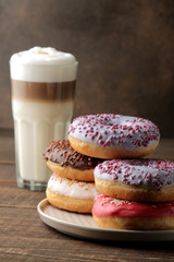 Assorted sweet donuts with icing and toppings, and coffee latte on a brown wooden table.