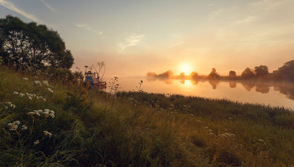 foggy dawn on the river bank with beams of a rising sun