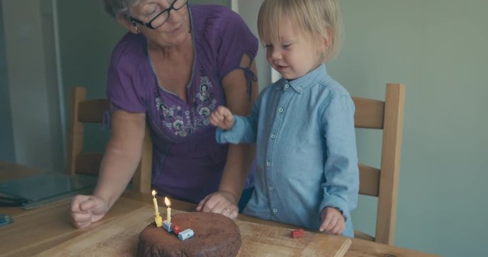 Grandmother helping toddler blow out candles