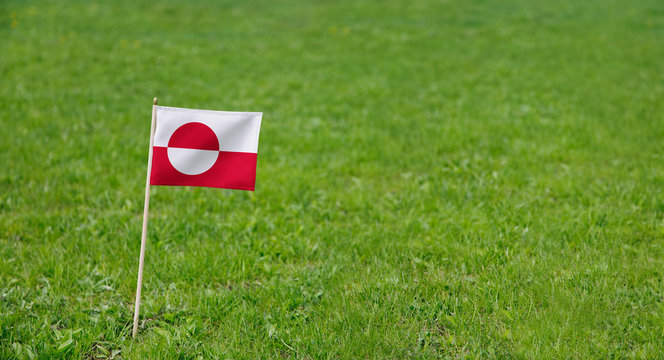 Greenland flag. Photo of Greenland flag on a green grass lawn background. Close up of national flag waving outdoors.