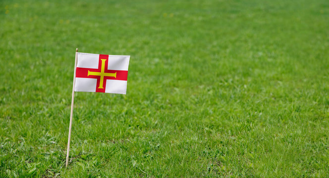 Guernsey flag. Photo of Guernsey flag on a green grass lawn background. Close up of national flag waving outdoors.
