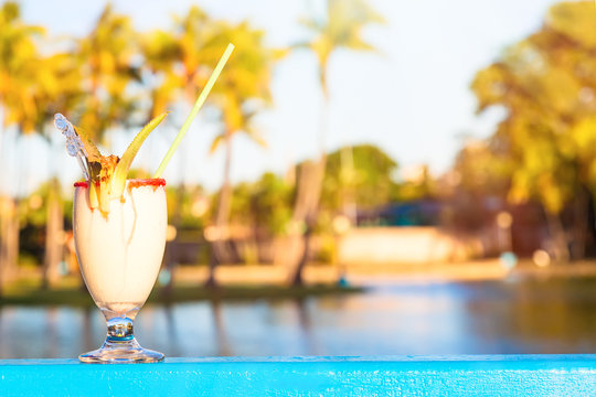 Refreshing pina colada cocktail against water and palm trees background. Summer vacation concept.