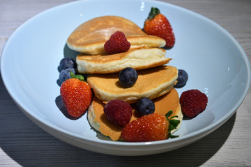 Japanese fluffy pancakes with berries on top on white wooden table.