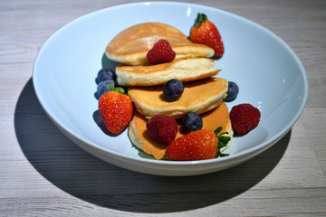 Japanese fluffy pancakes with berries on top on white wooden table.