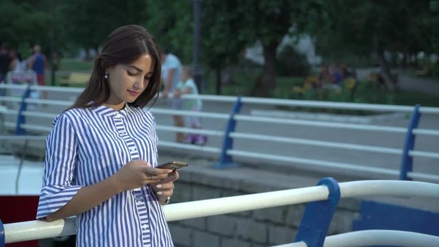 Attractive young woman surfing the net on her phone standing on a river quay  
