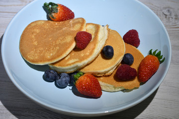Japanese fluffy pancakes with berries on top on white wooden table.