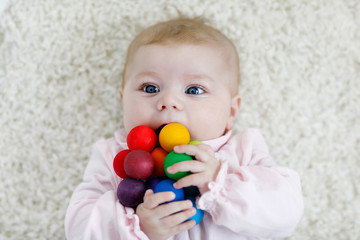 Fototapeta na wymiar Cute adorable newborn baby playing with colorful wooden rattle toy ball on white background. New born child, little girl looking ath the camera. Family, new life, childhood, beginning concept.