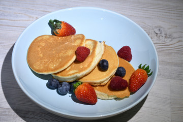Japanese fluffy pancakes with berries on top on white wooden table.