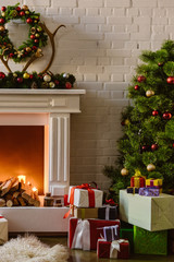 christmas tree with festive decorations and gift boxes near fireplace with firewood in living room