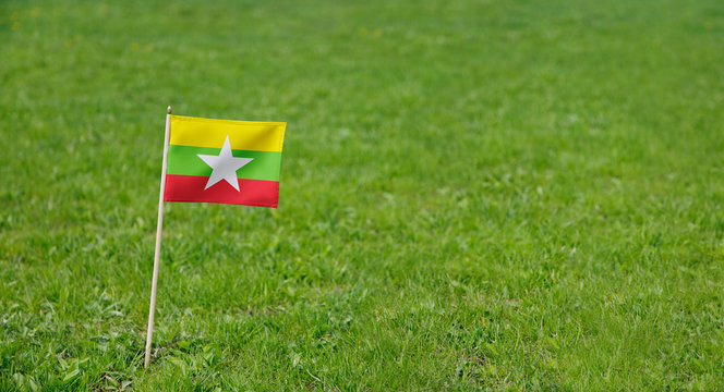 Myanmar flag. Photo of Myanmar flag on a green grass lawn background. Close up of national flag waving outdoors.