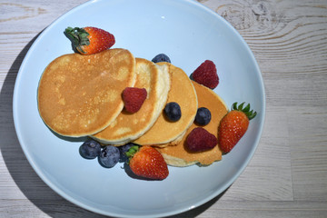 Japanese fluffy pancakes with berries on top on white wooden table.