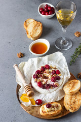 Baked camembert with cranberry, walnuts, honey and thyme on parchment paper. Brie type of cheese. Grey slate, stone or concrete table. Copy space.
