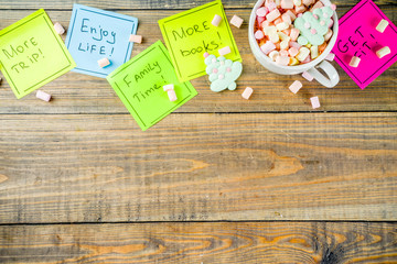 New years resolutions, colorful sticky notes with popular new year resolutions, wooden background with funny hot chocolate cup,  copy space top view flatlay