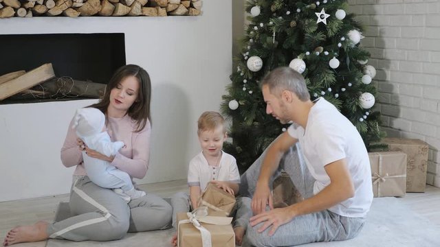 Cute family opening presents while sitting on floor near Christmas tree in cozy room