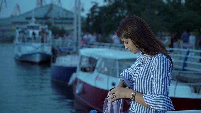 Glamour young woman seeking something in her purse standing on a river quay   