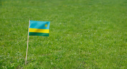 Obraz premium Rwanda flag. Photo of Rwandan flag on a green grass lawn background. Close up of national flag waving outdoors.
