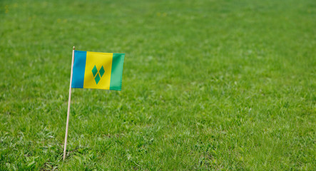 Saint Vincent and the Grenadines flag. Photo of a flag on a green grass lawn background. Close up of national flag waving outdoors.