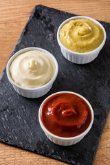Ketchup,mustard and mayonnaise in a bowls on black slate