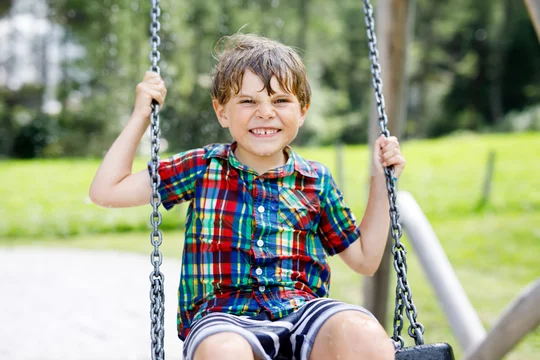 Funny kid boy having fun with chain swing on outdoor playground. child  swinging on warm sunny spring or autumn day. Active leisure with kids.  Selective focus, no face of kid. Stock Photo