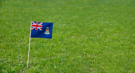 Cayman Islands flag. Photo of Cayman Islands flag on a green grass lawn background. Close up of national flag waving outdoors.