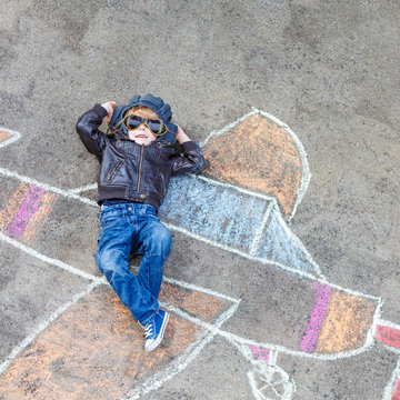 Funny little kid boy flying by a plane picture painting with colorful chalk. Creative leisure for children outdoors in summer