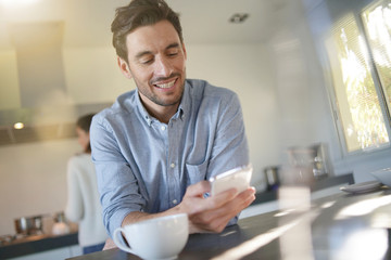  Relaxed handsome man in modern kitchen with wife in the background