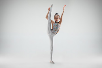 The teen female little girl doing gymnastics exercises isolated on a gray studio background. The...