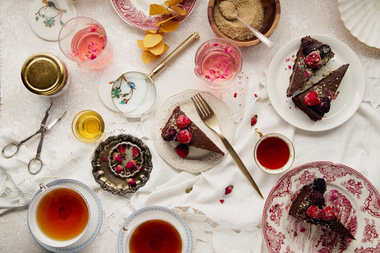 Overhead image of tea party with chocolate cheesecake slices with raspberry on various plates. Traditional style, vintage tablecloth and cutlery.