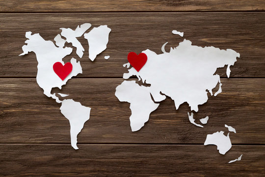 Red felt hearts and world map cutted from white paper on the wooden background. Long-distance relationships concept - Europe and United States. Flat lay, top view, copy space, mock up