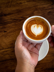 Girl holding cup of cafe latte on wooden table