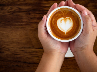 Girl holding cup of cafe latte on wooden table