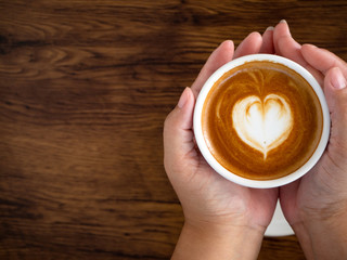 Girl holding cup of cafe latte on wooden table