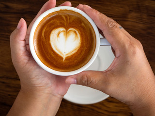 Girl holding cup of cafe latte on wooden table