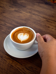 Girl holding cup of cafe latte on wooden table