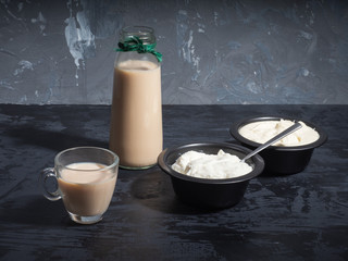 Breakfast of dairy products of milk, sour cream and cottage cheese on a dark background, glass mug and bottle, a teaspoon