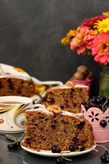 Homemade pie with black currant and walnuts is located on a plate on a dark background