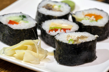 Sushi rolls on a white plate with soy sauce. Against the backdrop of a vintage wooden table.